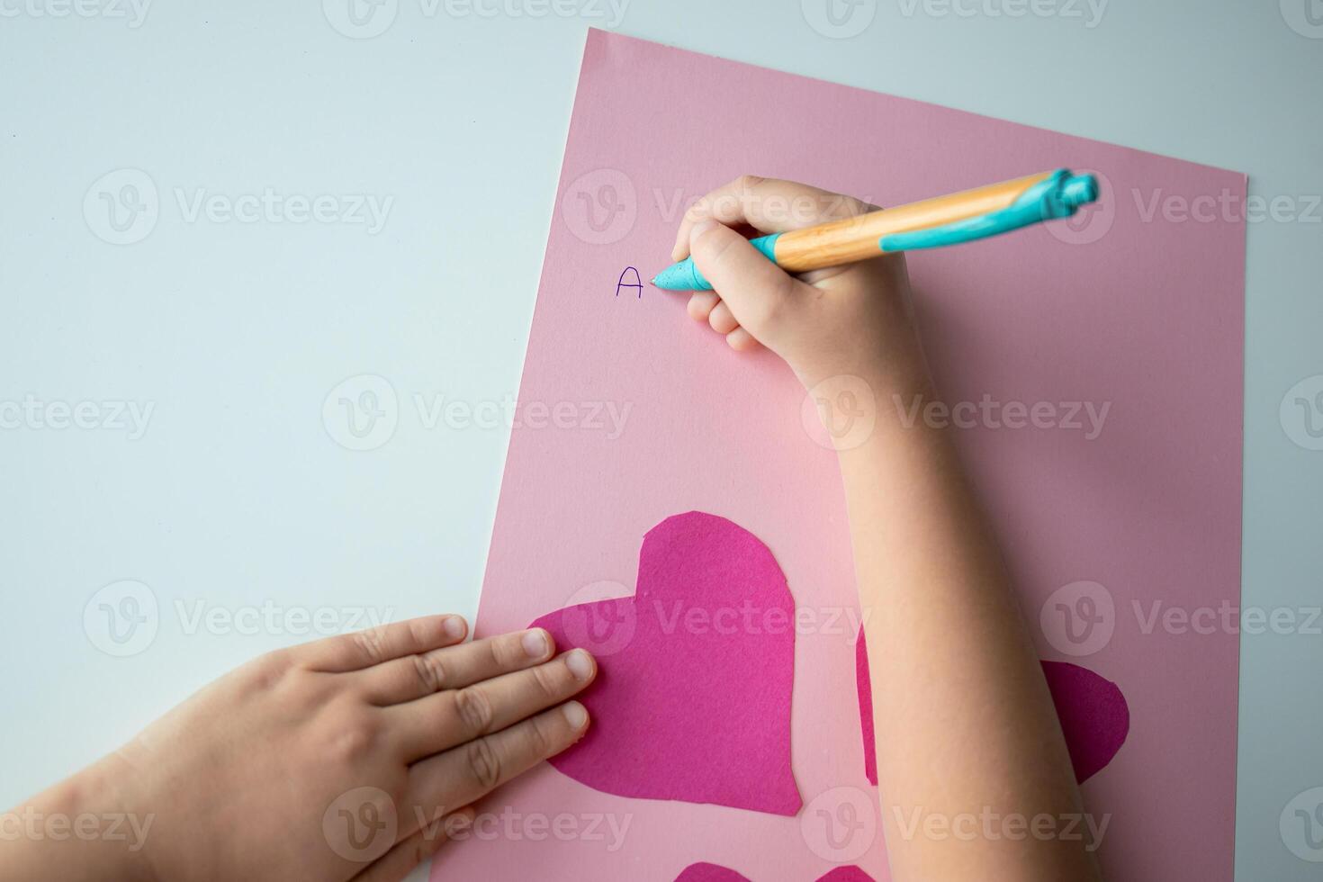 Child making heart shaped card with pink paper and letters photo