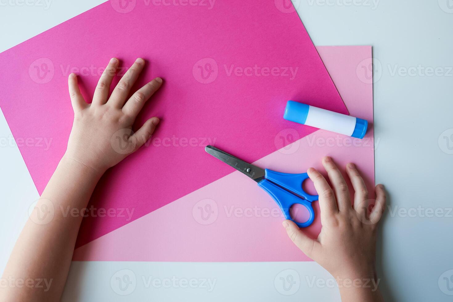 Child handcrafting with pink paper, scissors, and glue photo