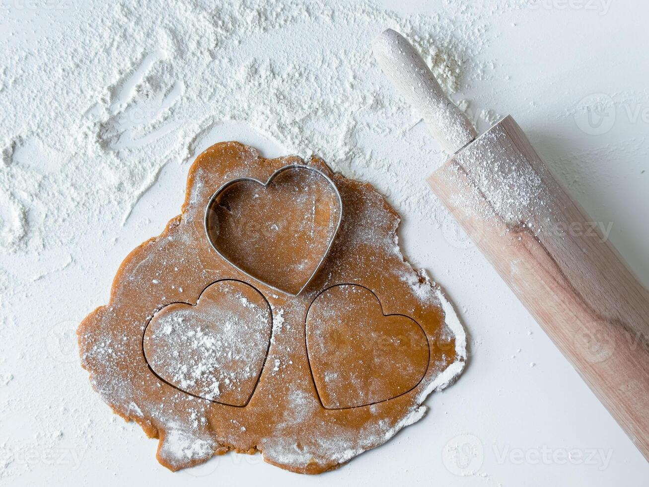 Heart shaped cookie cutouts on floured dough with rolling pin photo