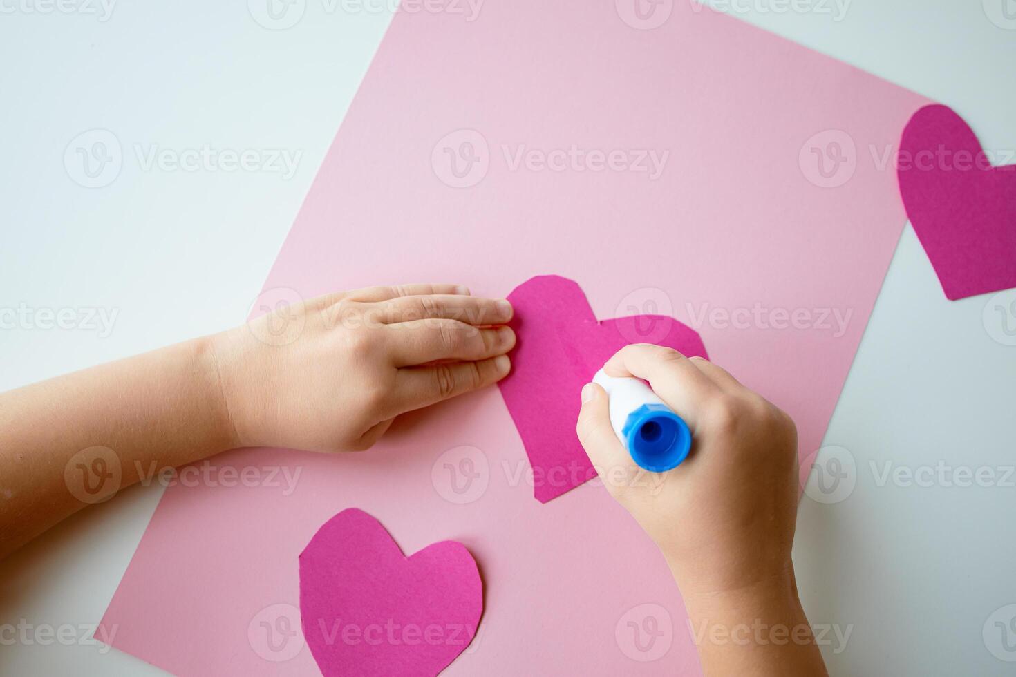 Child gluing pink paper hearts on craft project photo