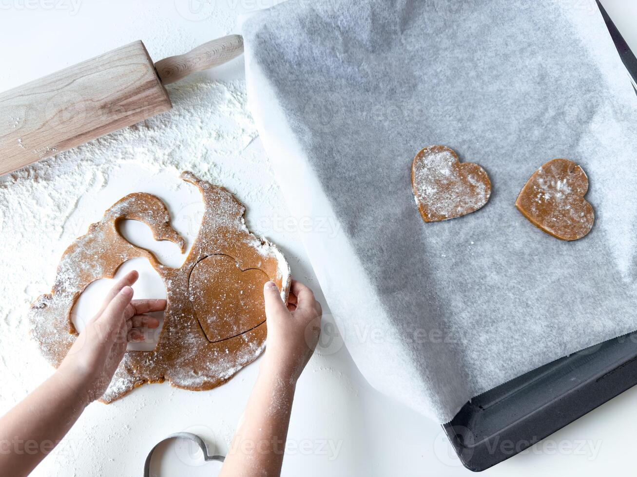 Child baking heart shaped cookies on a floured surface photo