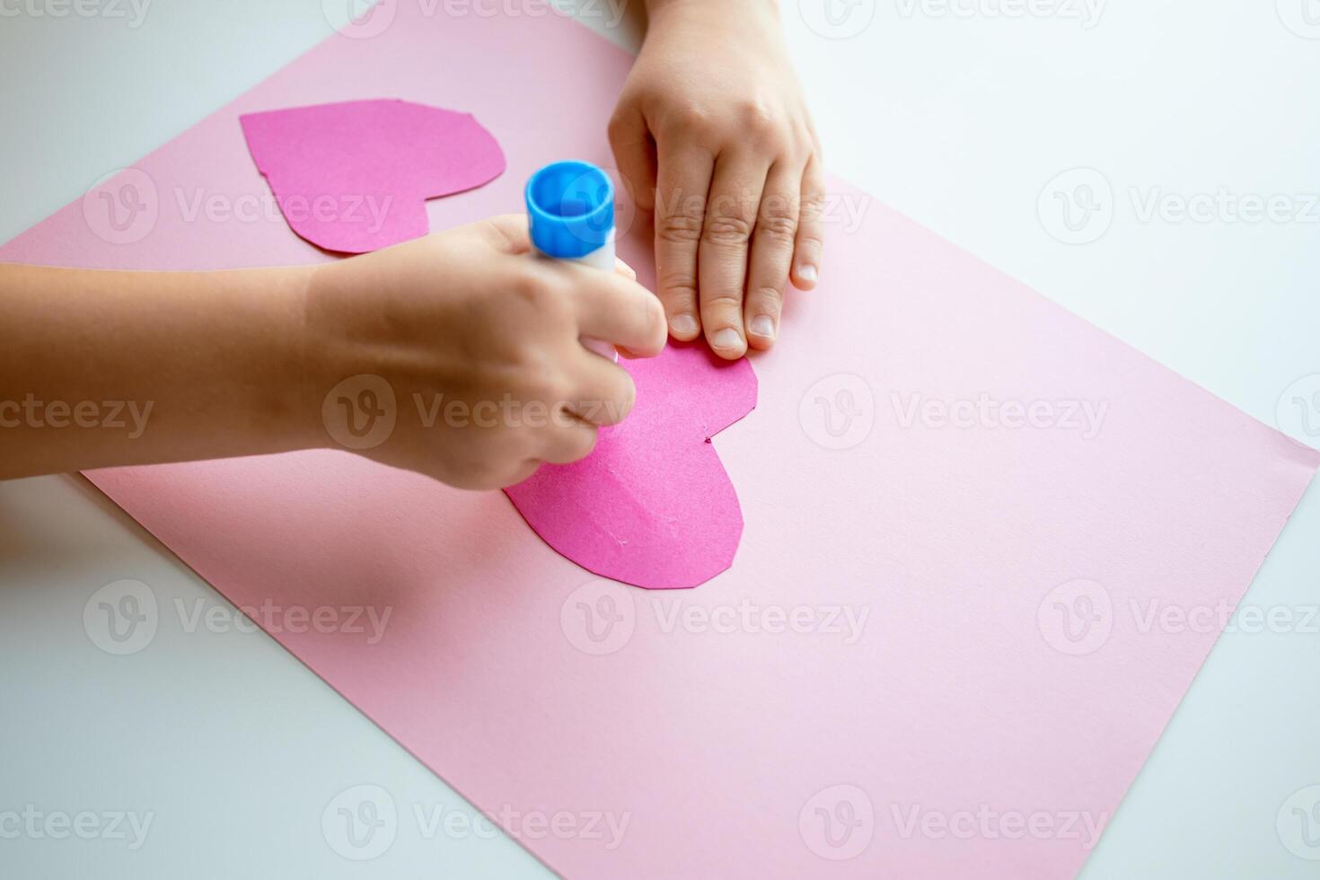 Child making heart shaped craft with pink paper and glue stick photo