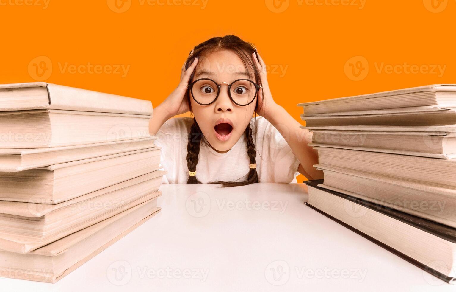 Too Much Homework. Shocked Overworked Asian Schoolgirl Cupping Head In Hands Sitting Between Two Books Stacks Over Yellow Studio Background. photo