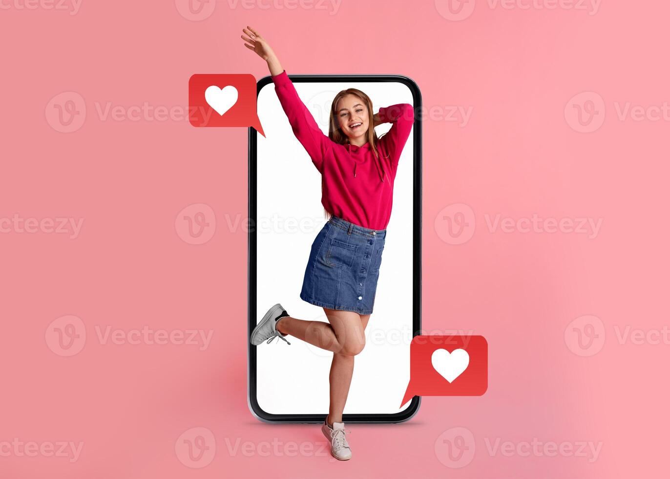 A young woman celebrates Valentine's Day, playfully posing with a smartphone. Bright pink background highlights the themes of love and social media in modern communication. photo