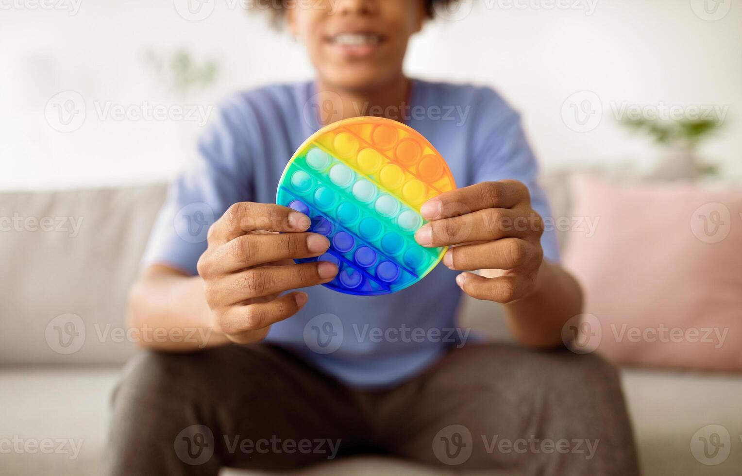 Cropped view of Afro teen guy playing with antistress POP IT toy indoors, closeup of hands. Unrecognizable black youth using sensory plaything at home. Stress relief, relax concept photo