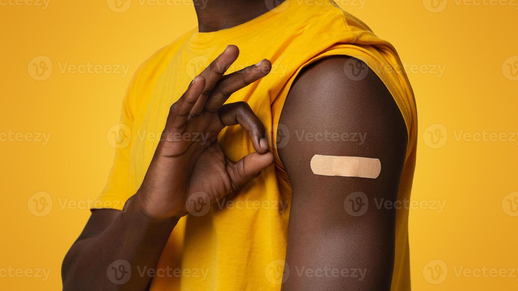 Closeup Shot Of Black Male Demonstrating Adhesive Bandage On Shoulder And Showing Ok Gesture, Unrecognizable African American Guy Recommending Vaccination Against Coronavirus, Cropped Image photo