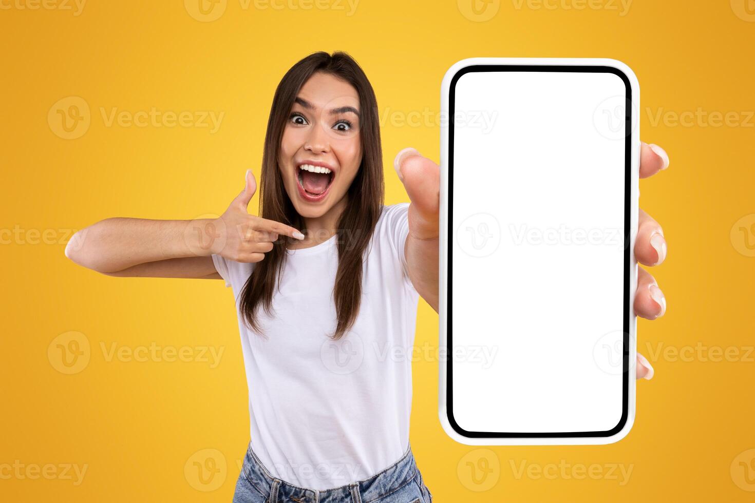 Great Mobile Offer. Excited Lady Pointing Finger At Smartphone In Her Hand, Emotionally Reacting To New App, Overjoyed Millennial Woman Standing Isolated Over Orange Studio Background, Panorama photo