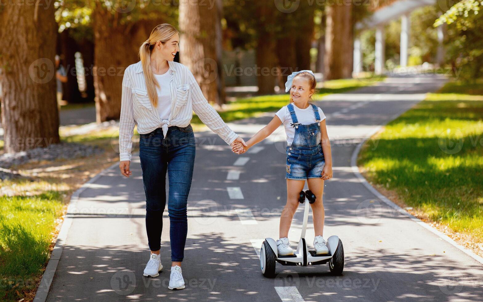 Happy Mom Teaching Little Daughter To Ride Segway Enjoying Day In City Park. Family Fun On Weekend. photo
