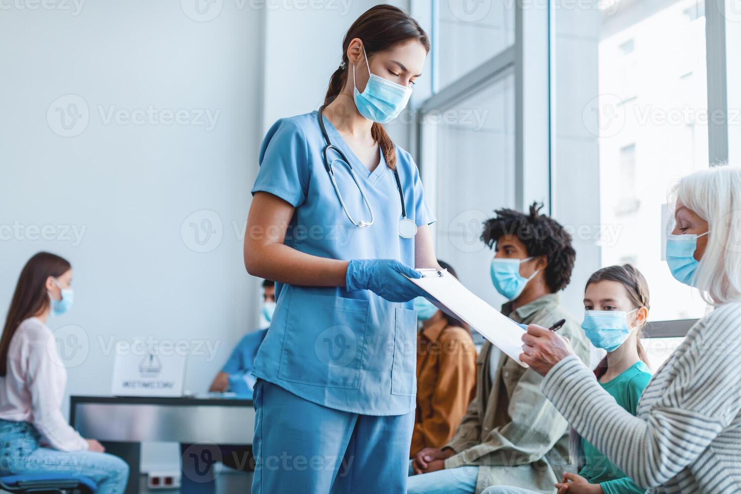 Diverse people waiting in line to get shots or to get tested for flu infection at the hospital. Senior patient signing Informed Consent for Vaccination against pneumonia, influenza or coronavirus photo