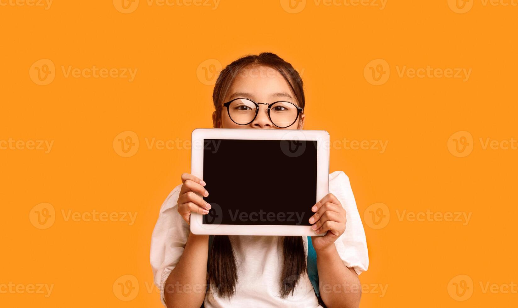 Online Class. Japanese Schoolgirl Showing Digital Tablet Blank Screen Recommending Educational Application Standing Over Yellow Studio Background photo