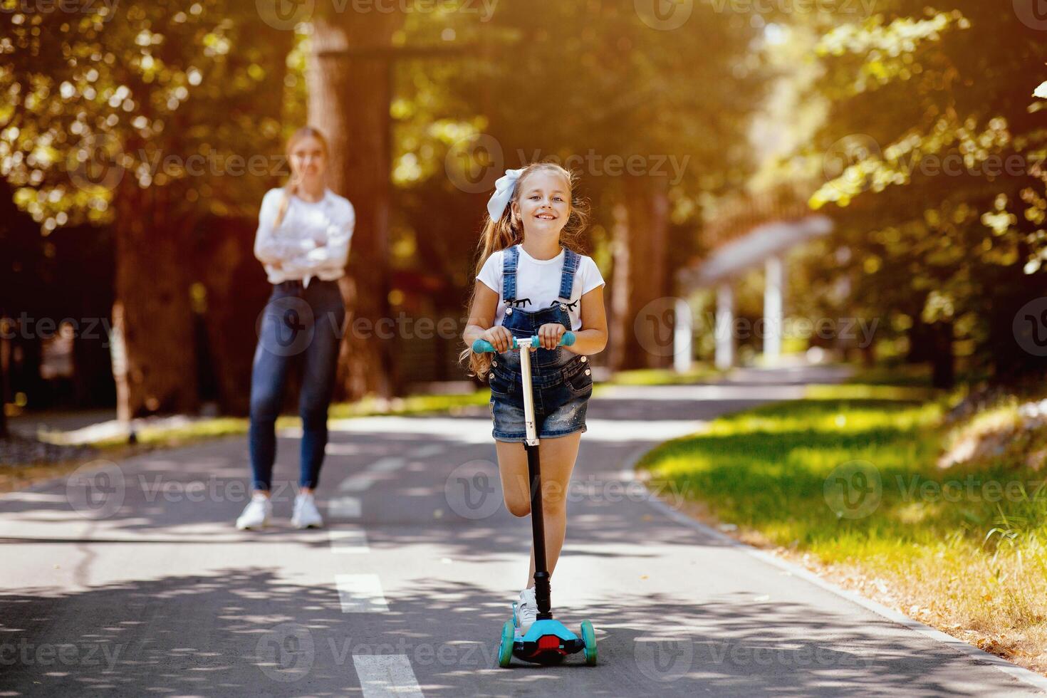 Little Girl Riding Kick Scooter Spending Weekend With Mother In City Park Outdoors. Summer Activity Concept. Selective Focus photo
