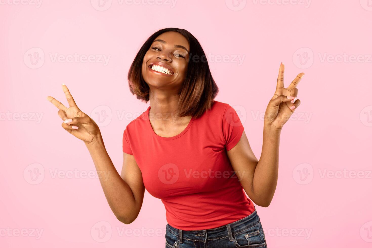 Toothy African American Woman Gesturing V-Sign Victory Symbol To Camera Posing Over Yellow Background. Studio Shot Of Female Showing Peace Gesture With Both Hands Concept photo