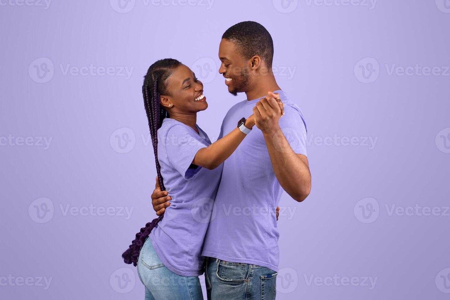 Romance Concept. Profile side view portrait of beautiful black couple in love dancing and looking at each other. Smiling young bearded guy hugging his pretty excited lady with long braids, violet wall photo