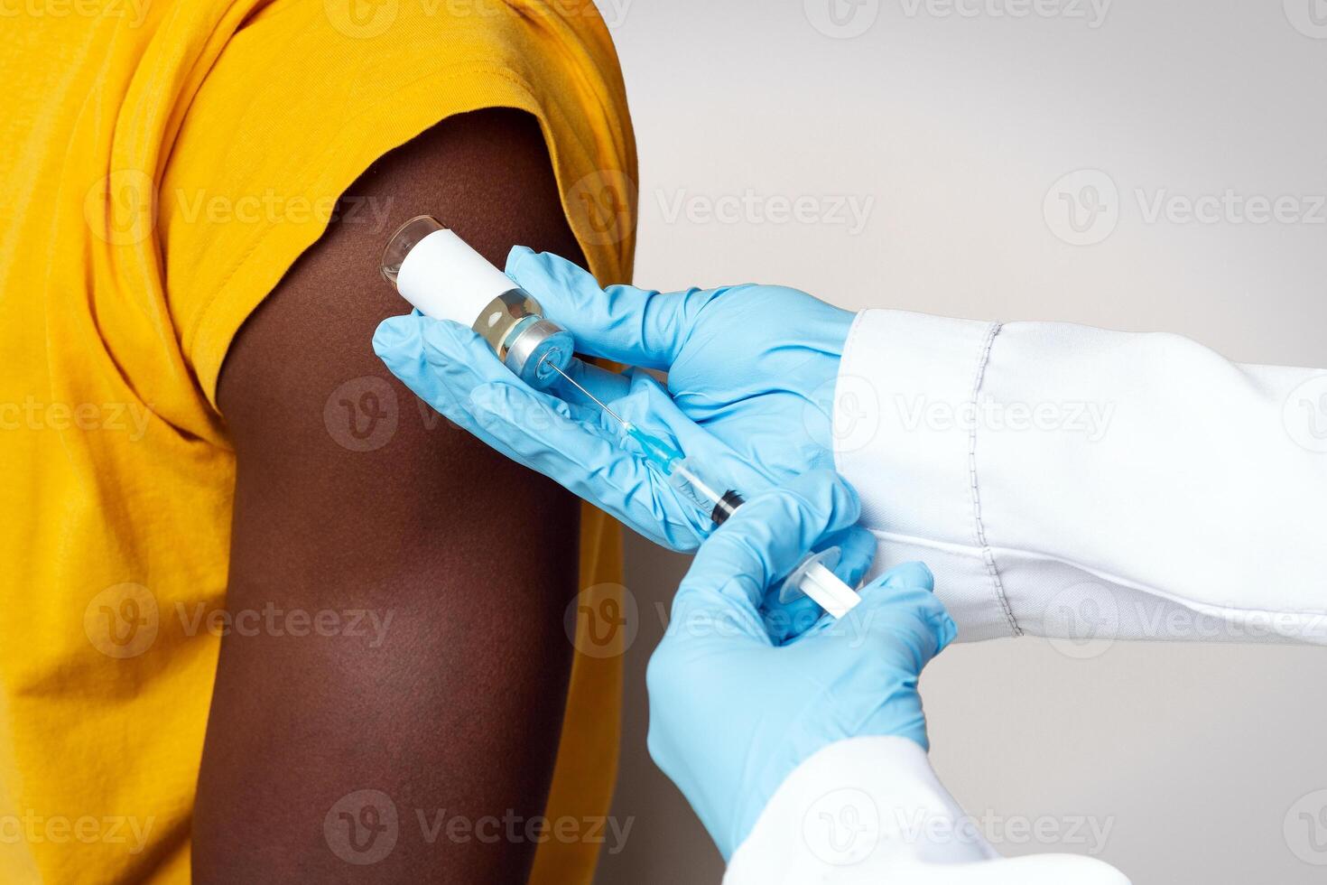 Unrecognizable Doctor Wearing Blue Gloves Making Vaccination Shot To Black Male Patient In Hospital, Medical Worker Using Syringe, Taking Dose Of Vaccine From Vial, Cropped Image, Closeup Shot photo