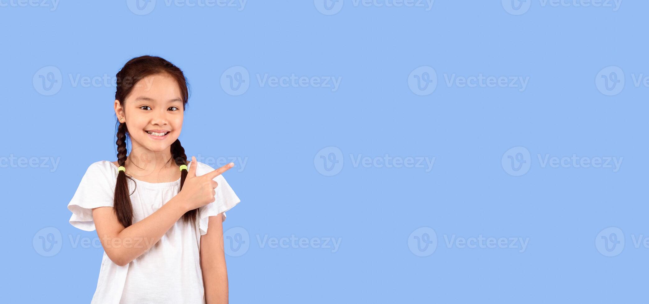 Look There. Cute Asian Little Girl Pointing Finger Aside At Empty Space Standing On Purple Background In Studio. Panorama photo