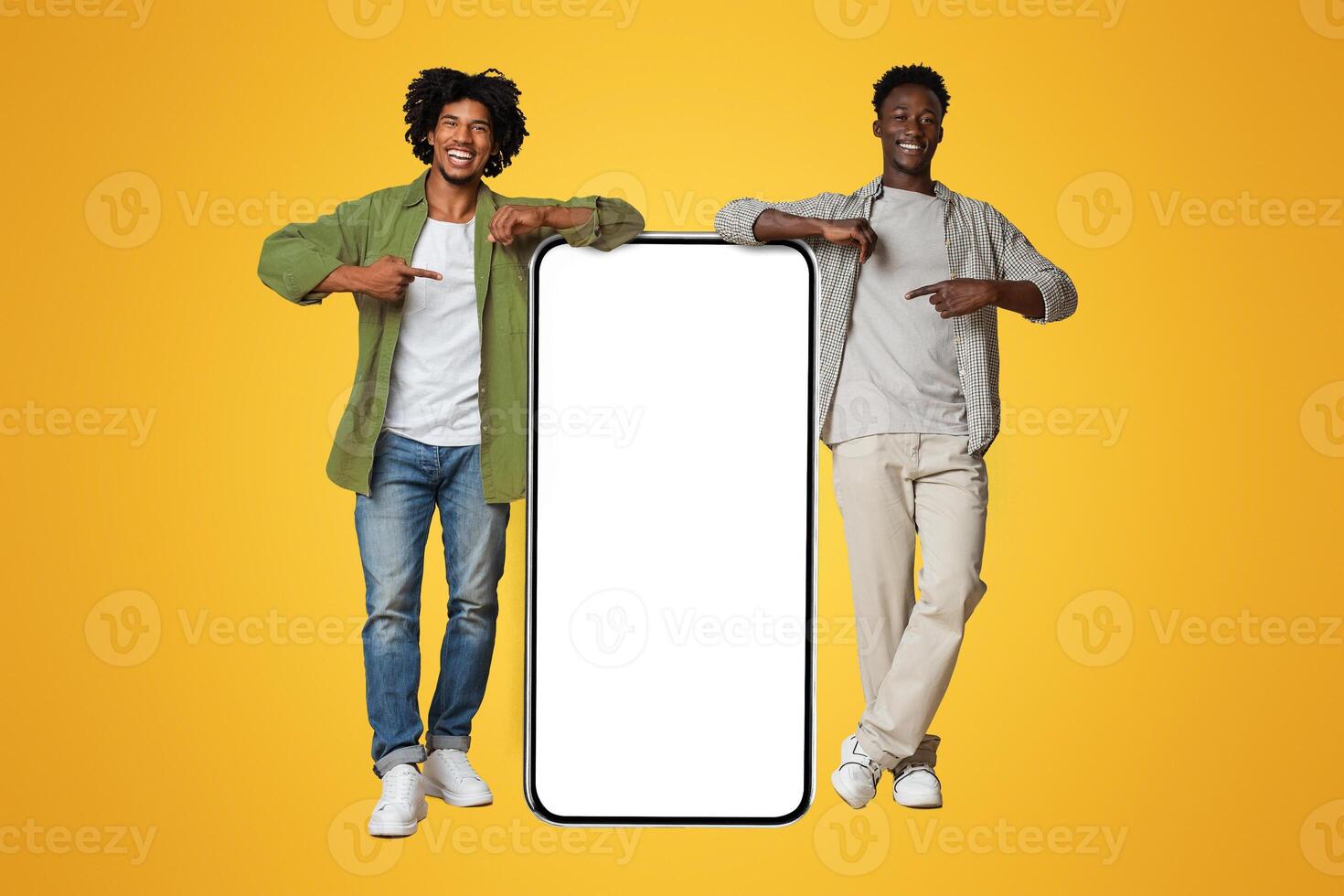 Mobile Ad. Two Black Guys Pointing At Big Smartphone With Blank White Screen, Excited African American Friends Showing Free Copy Space For App Design, Standing Over Beige Studio Background, Mockup photo