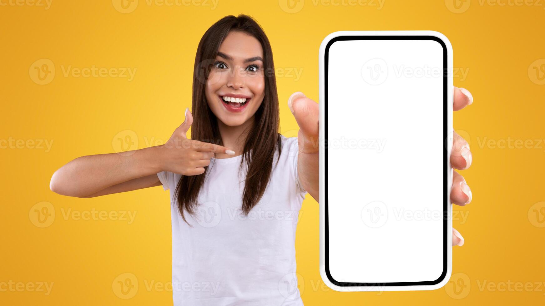 Mobile Advertisement. Excited Lady Pointing On Smartphone With Blank Screen, Emotional Surprised Woman Recommending New Application Or Website, Presenting Device Display On Orange Background, Mockup photo