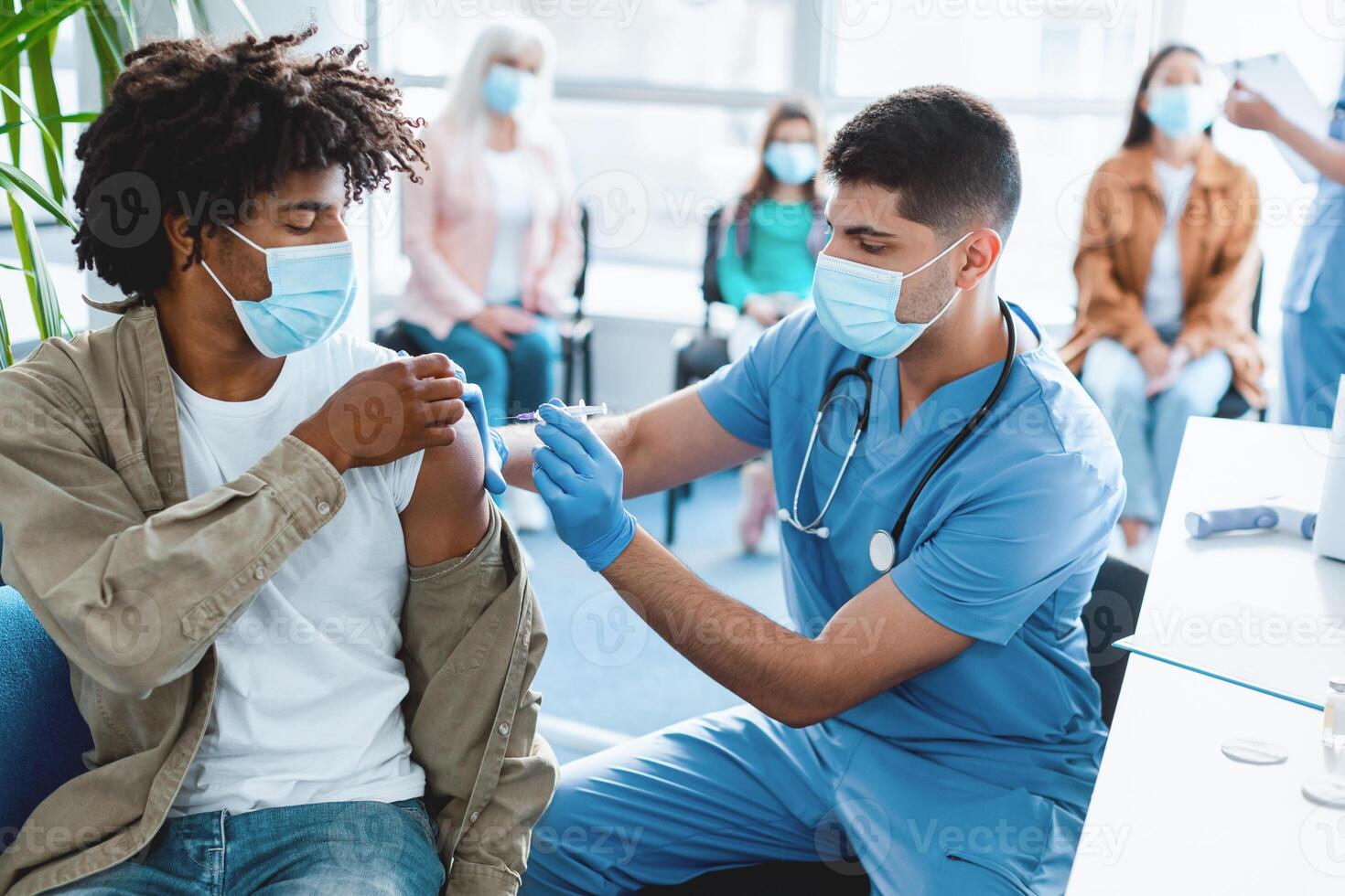 Doctor holding syringe making vaccination injection dose in shoulder of African American guy patient. Flu influenza vaccine clinical trials concept, corona virus treatment side effect, inoculation photo