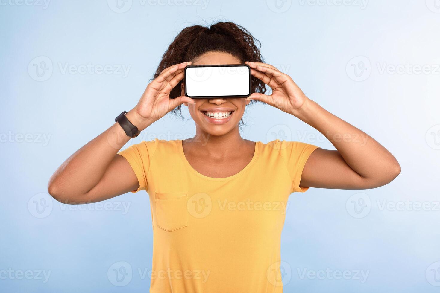 Cellphone screen mockup. Happy African American woman covering eyes with blank smartphone, recommending mobile app, advertising new website over blue studio background, space for ad design photo