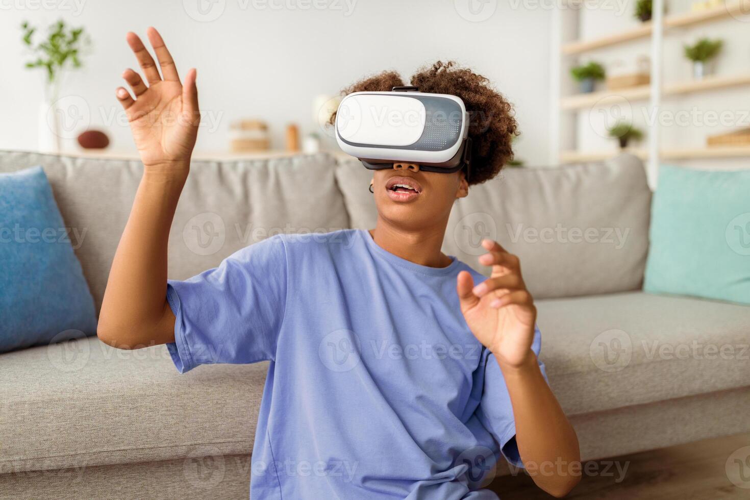 Modern domestic hobbies. African American teen guy in virtual reality headset touching imaginary screen, exploring cyberspace at home. Black adolescent in VR glasses playing interactive game photo