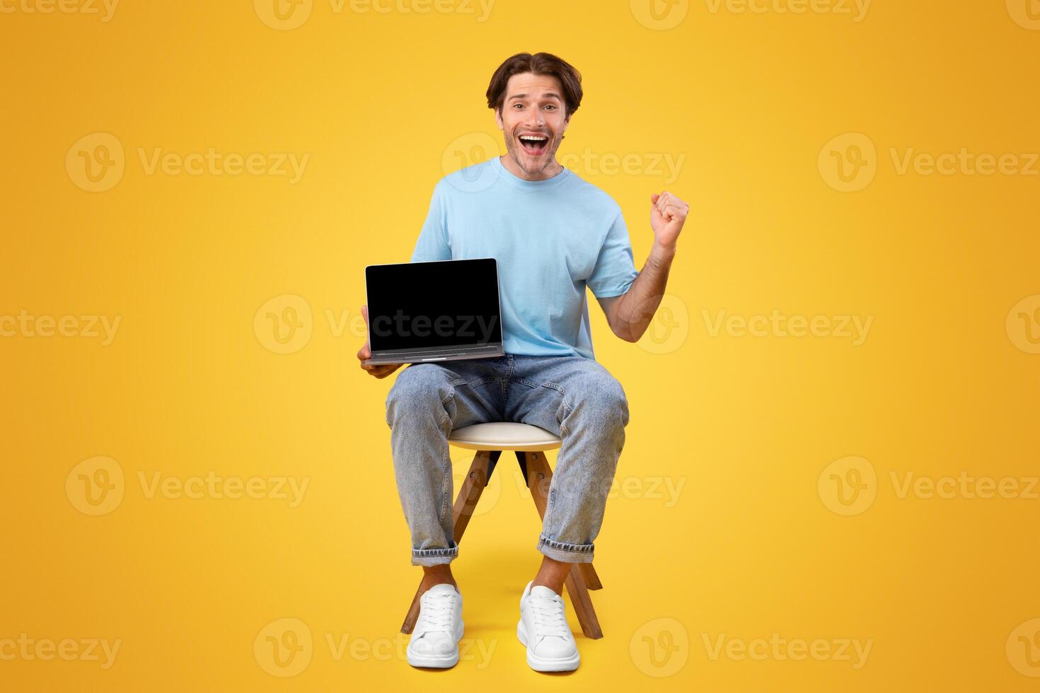 Online Win. Vertical portrait of excited happy guy holding pc laptop with black blank screen, shaking clenched fist making winner gesture, screaming yes showing device with empty free space for mockup photo