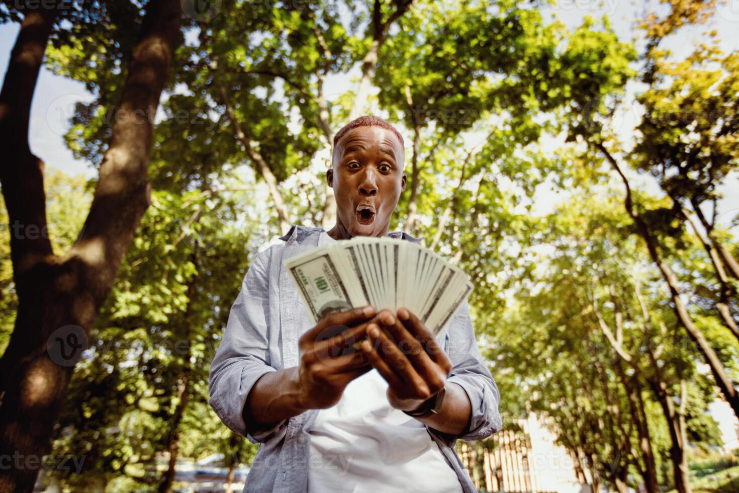 Shocked black guy with huge fan of money at city park photo