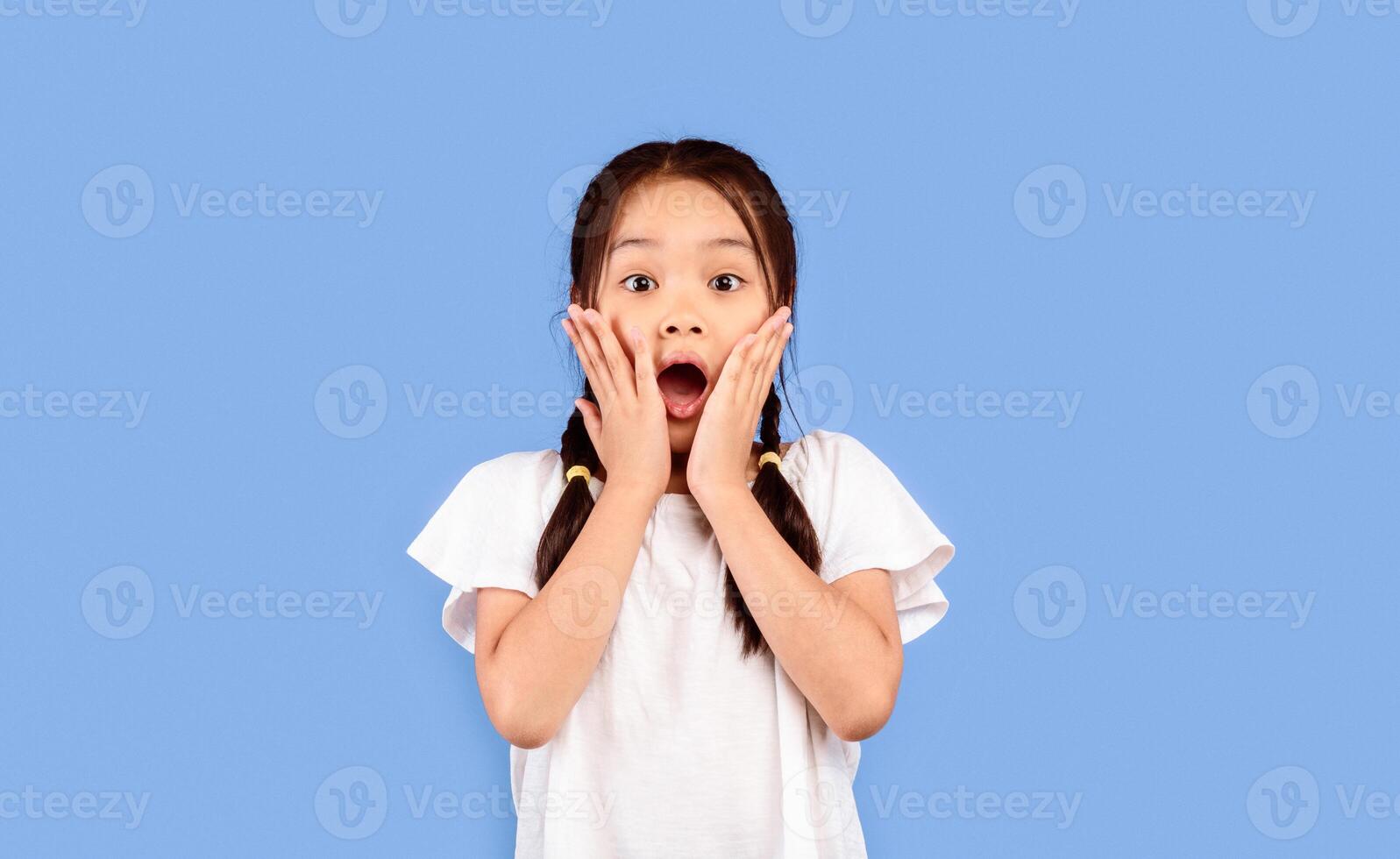 Omg. Shocked Asian Kid Girl Touching Face Looking At Camera In Amazement Standing Over Purple Background. Studio Shot photo