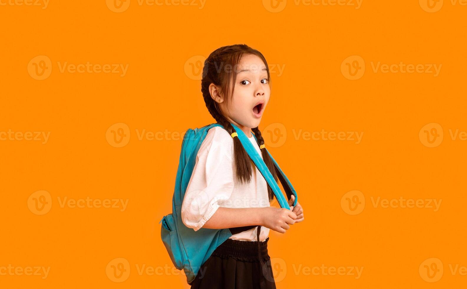 Shocked Asian Schoolgirl Looking At Camera With Opened Mouth Posing Over Yellow Background. Studio Shot, Free Space photo