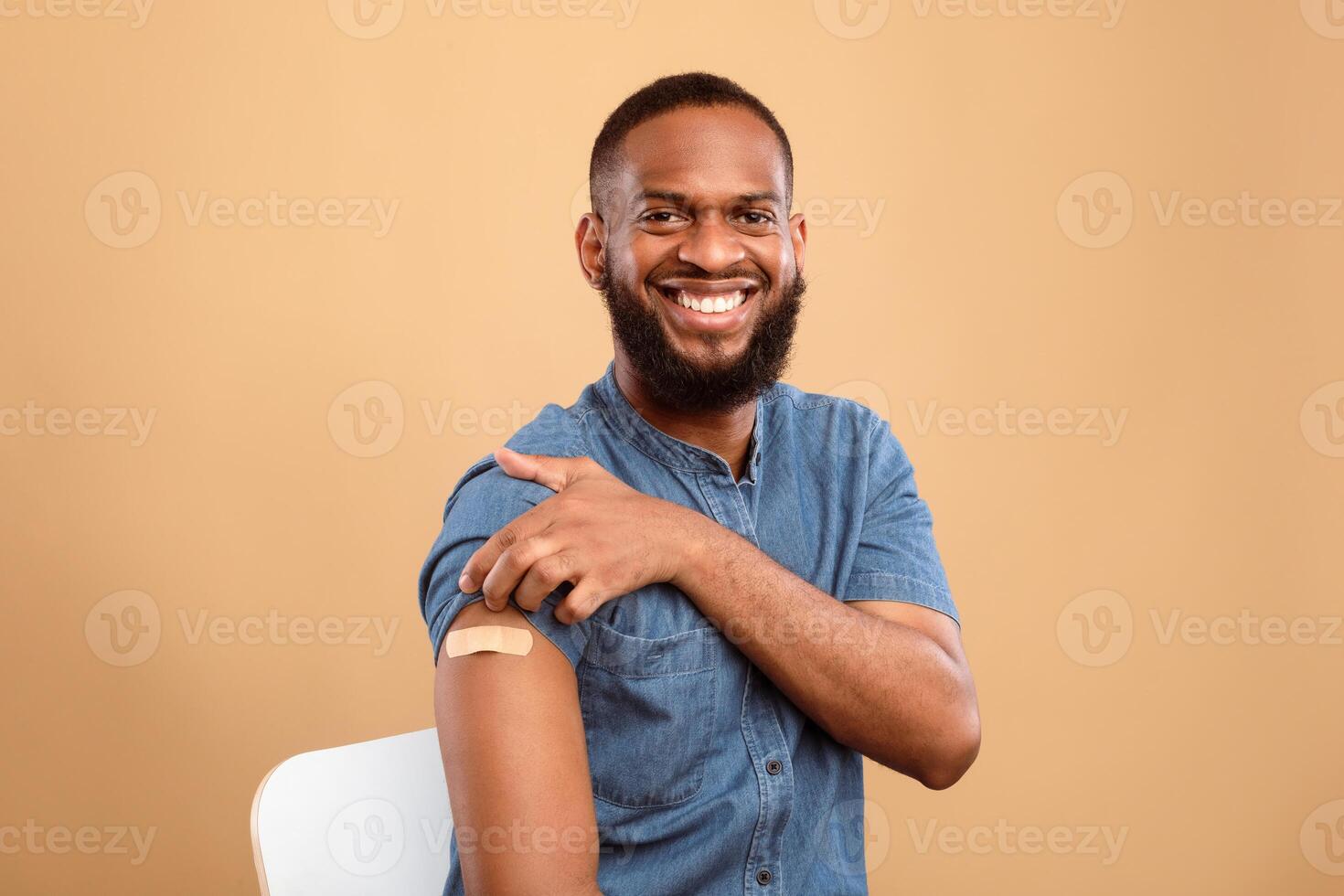 Antiviral immunization. Cheerful vaccinated African American man showing shoulder with medical band aid after flu vaccine shot, posing after flu vaccination, beige studio background photo