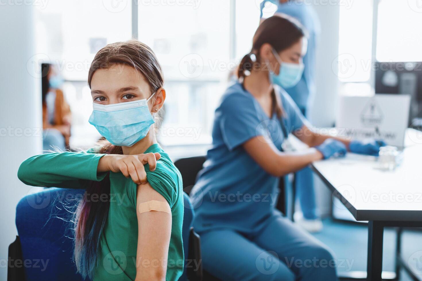 flu Vaccination Concept. Happy Adolescent Girl In Surgical Mask Showing Vaccinated Arm With Adhesive Bandage Plaster On Shoulder After Getting Corona Virus Vaccine In Clinic. Antiviral Injection photo