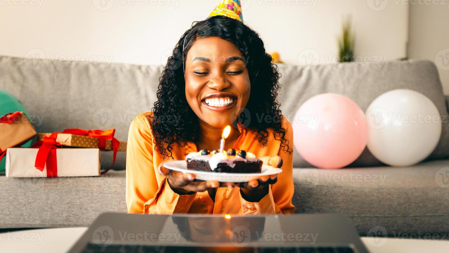Joyful Black Woman Holding Birthday Cake In Front Of Laptop Having Celebratory Call Partying Online, Celebrating Her Holiday Remotely At Home. Distance B-Day Celebration Concept photo