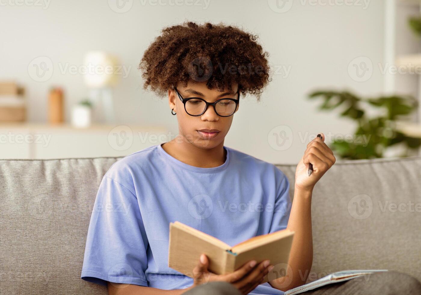 Serious black youth with textbook taking notes, studying at home, getting ready for exam. Intelligent African American teenager learning remotely during coronavirus isolation photo