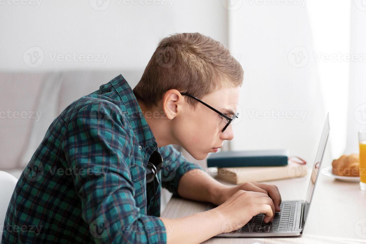 Concentrated nerd boy using laptop, working on project at home, empty space photo