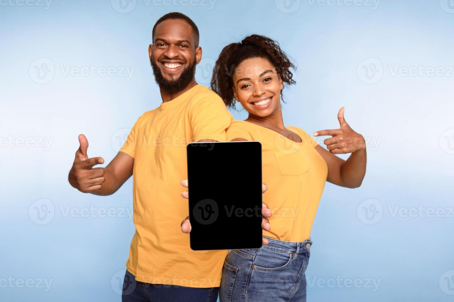 Cheerful African American couple holding tablet pc together, pointing at empty screen with space for mockup, promoting new application, website, advertising your product, blue background. photo