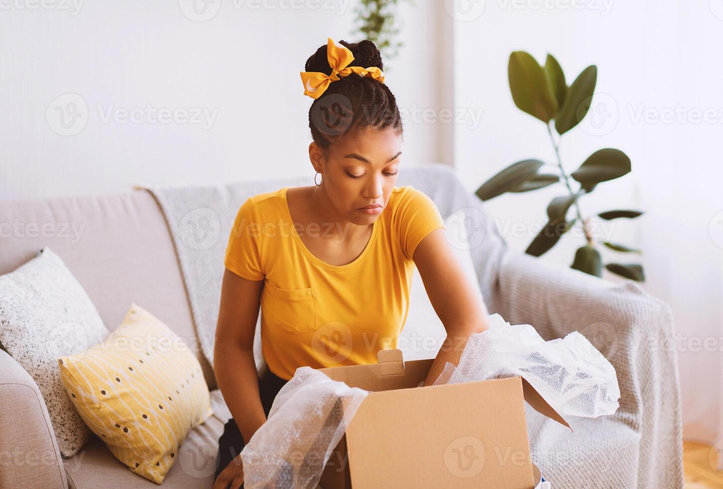 Wrong Package. Portrait of confused and dissatisfied african american woman unpacking box and looking inside, not happy by bad delivery service sitting on sofa at home. Shipping mistake, copy space photo