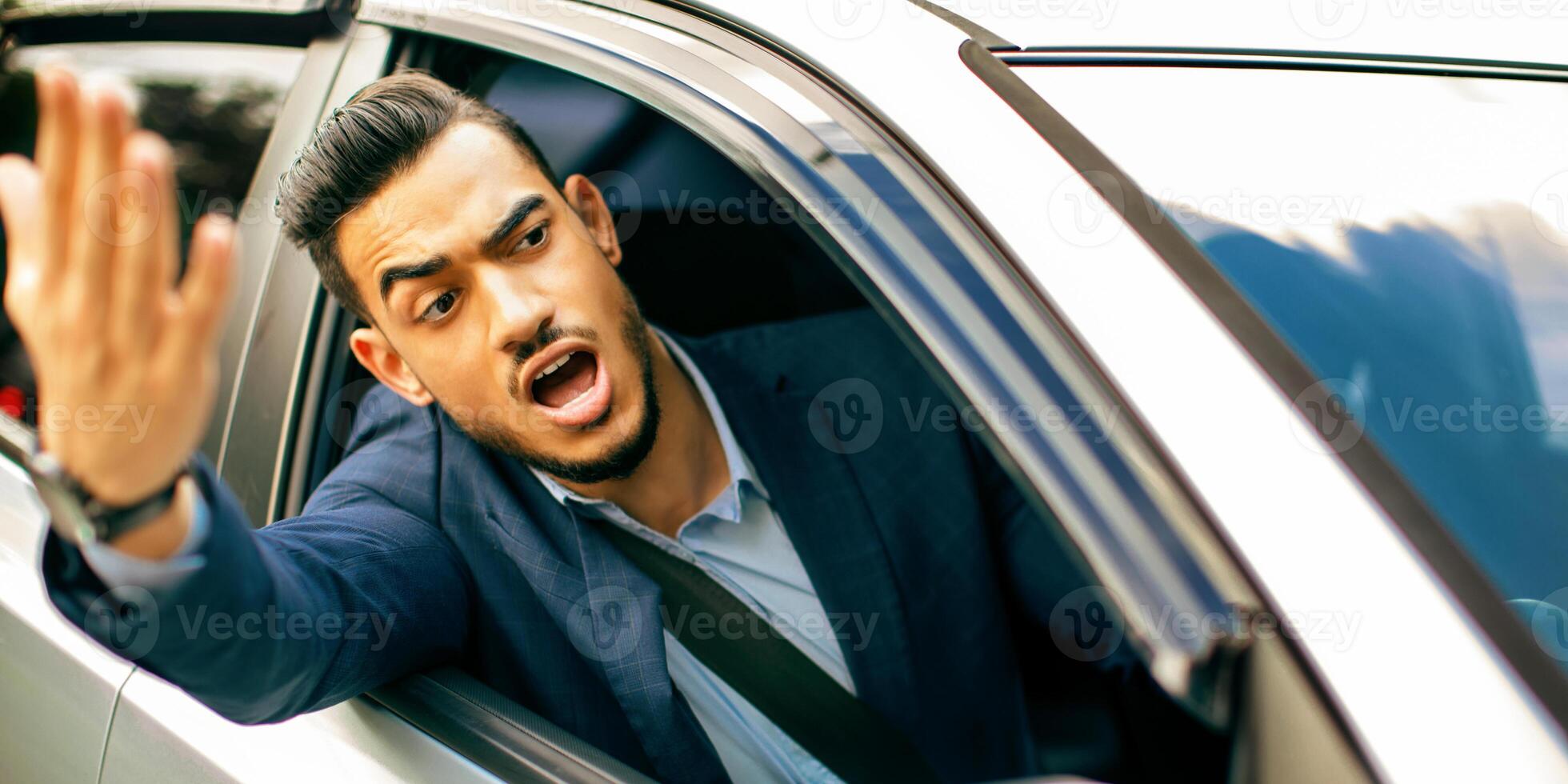 Furious middle-eastern businessman driving car, fighting with other drivers on road, emotional arab man getting late for business meeting or flight, stuck in traffic, yelling and gesturing photo