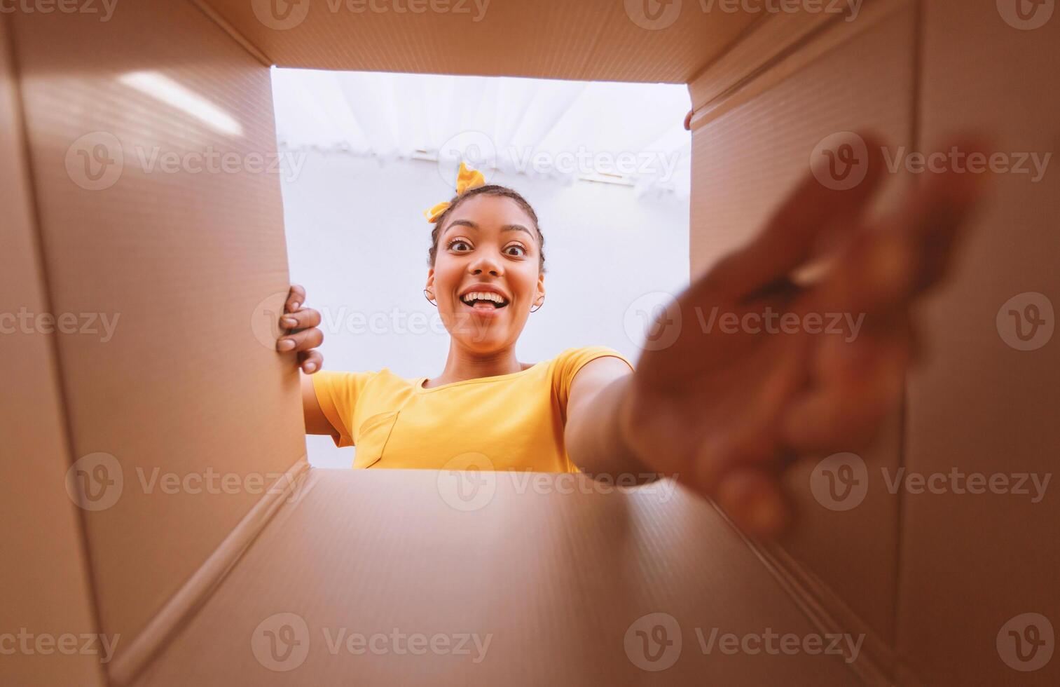 Home Delivery Service And Unboxing Concept. Happy and excited african american woman unpacking carton box and looking inside, trying to get goods outside. View from the package on overjoyed black lady photo