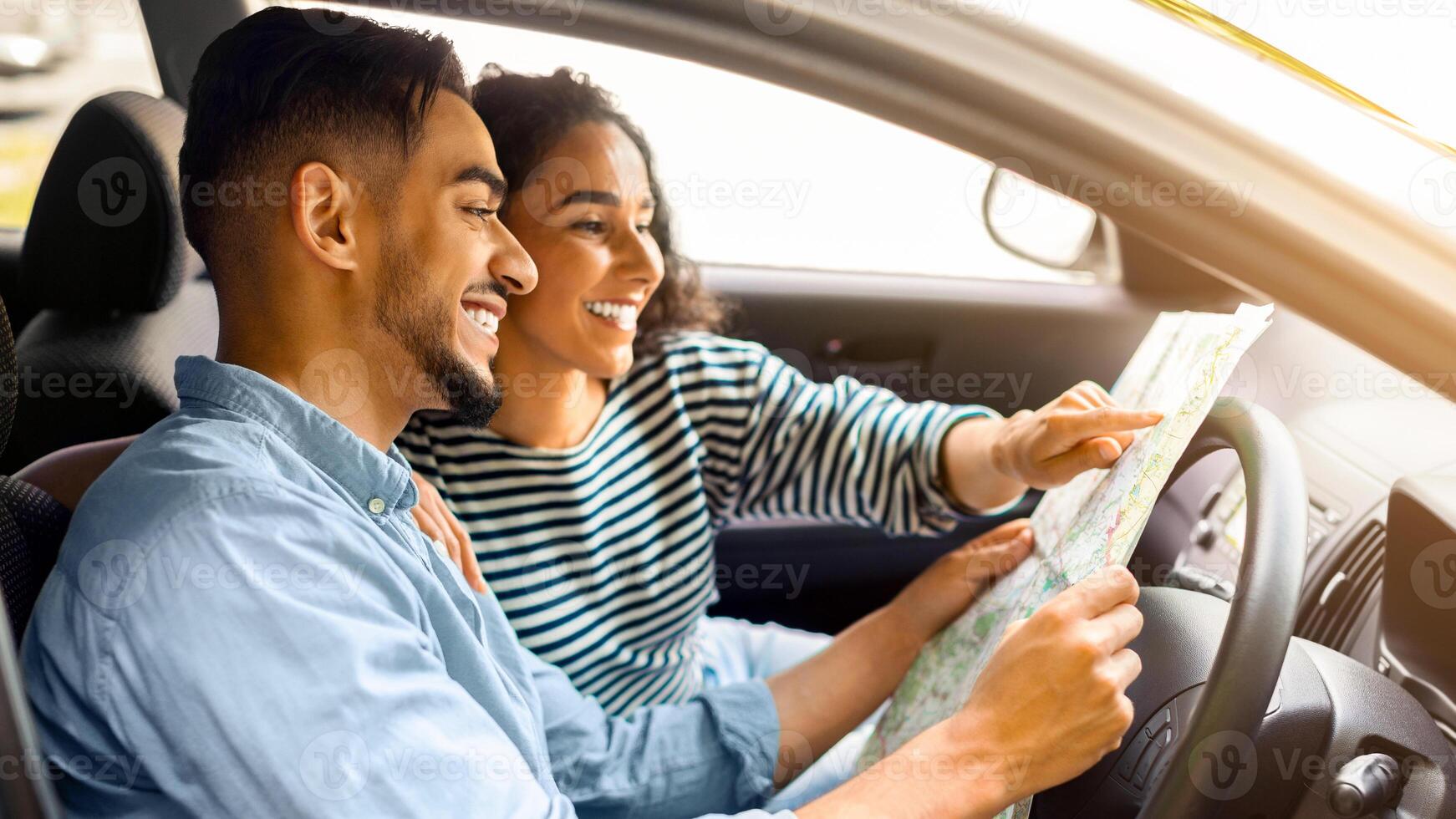 Happy young arab man and woman having car trip together, reading map and smiling, side view, copy space. Cheerful international couple enjoying journey by cozy auto, tracking their way photo