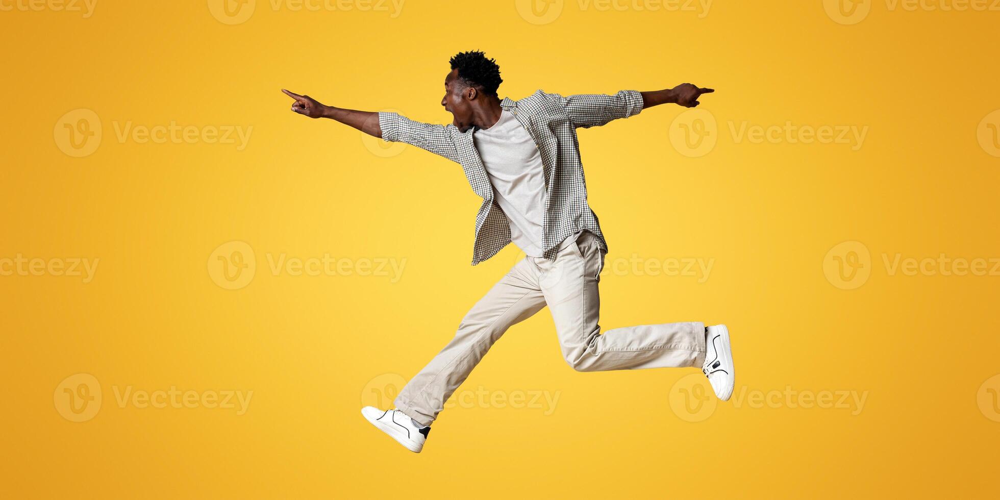 Crazy Sales. Excited black guy jumping up in air and pointing aside at copy space on beige background, emotional young african man demonstrating free place for design or advertisement, panorama photo
