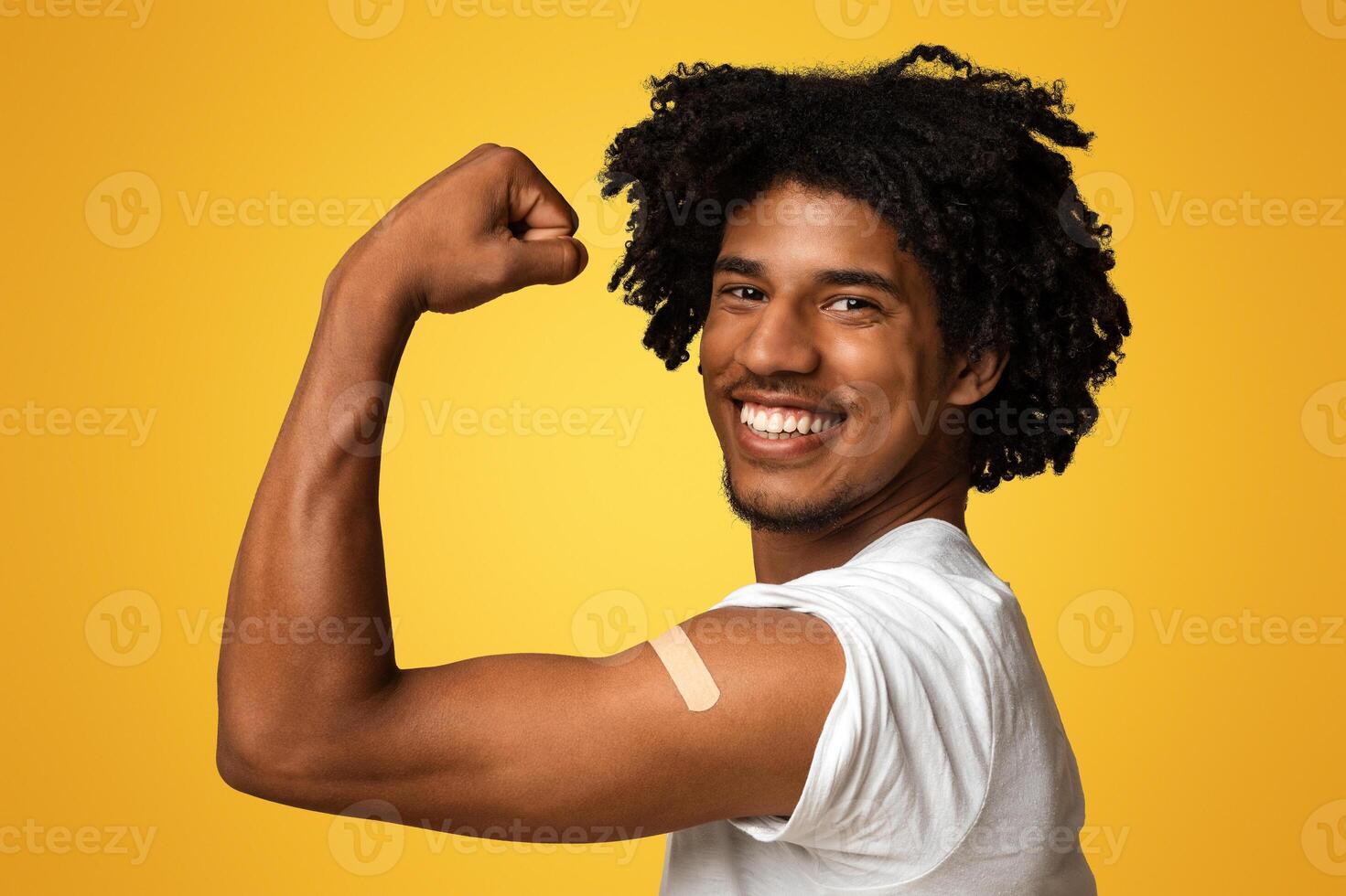 Excited African American Man Showing Arm With Plaster After Getting Covid-19 Vaccination, Happy Vaccinated Black Guy Demonstrating Biceps With Adhesive Band, Posing Over Beige Studio Background photo