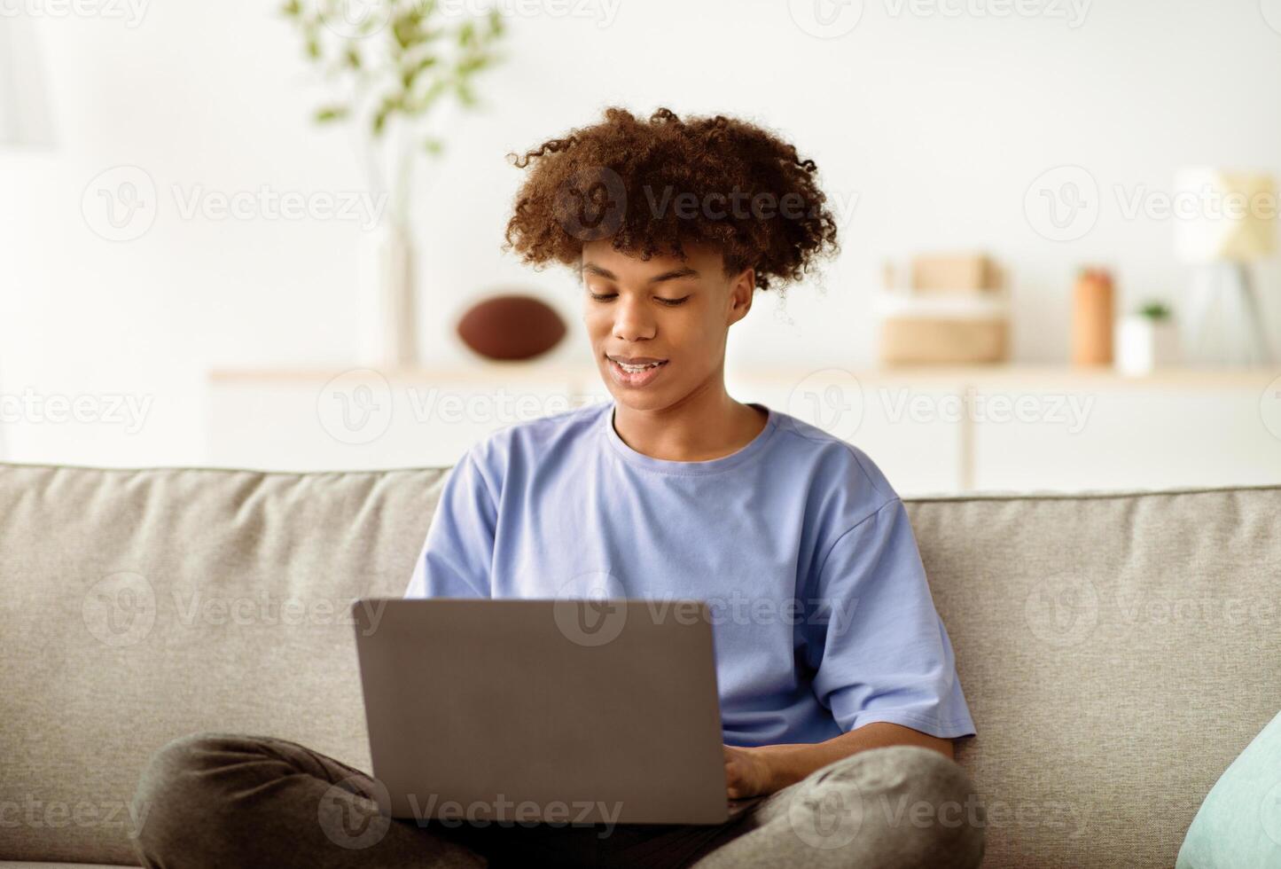 Home schooling. Attractive black teenage guy having online class, using laptop, talking to fellow students or teacher indoors. Positive adolescent taking part in webinar, attending lecture on pc photo