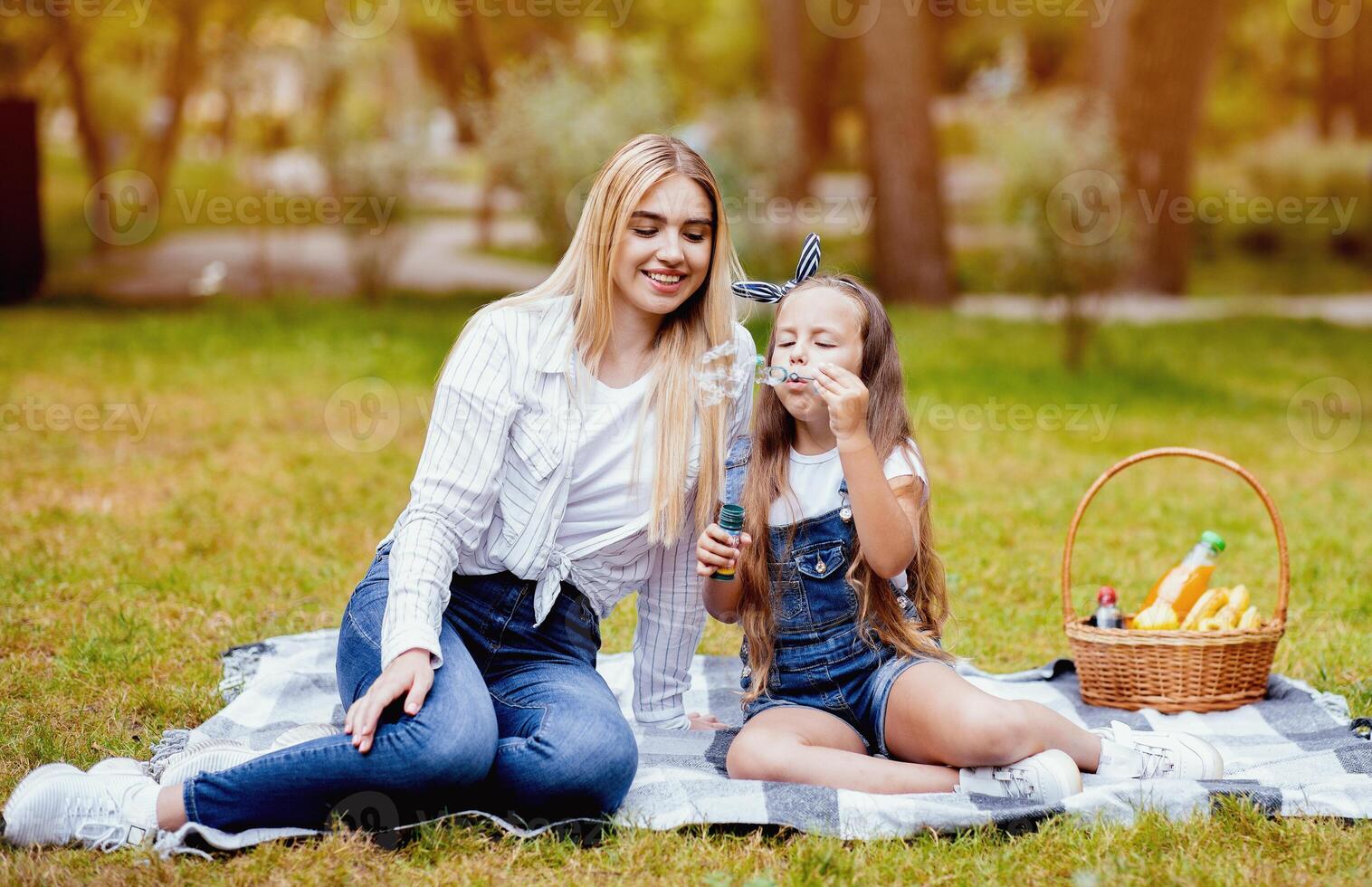 Summer Picnic Concept. Smiling Mother And Daughter Blowing Soap Bubbles Having Fun Relaxing Outdoor In Park. photo