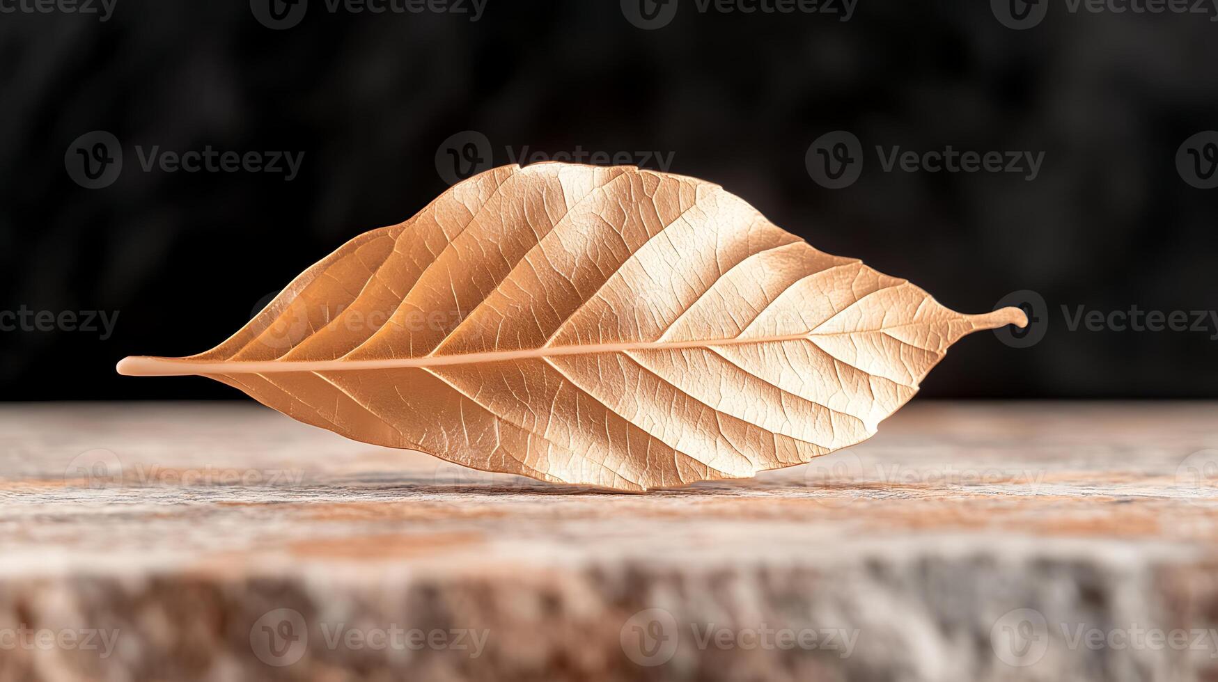 A beautifully crafted golden leaf resting on a textured stone surface with a blurred dark background photo
