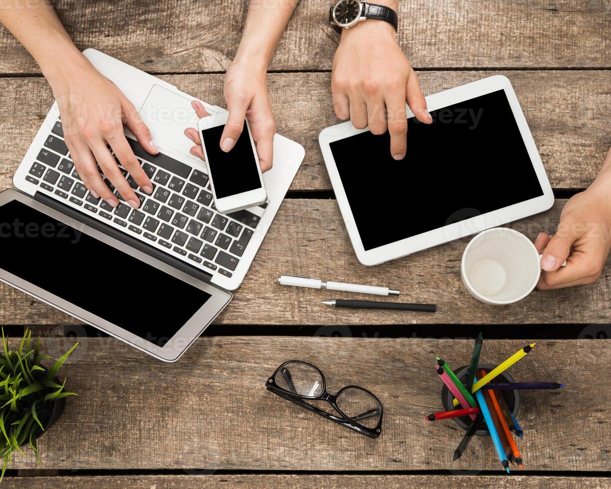 People engaging with various devices while working at a wooden table in a co-working space during daytime photo