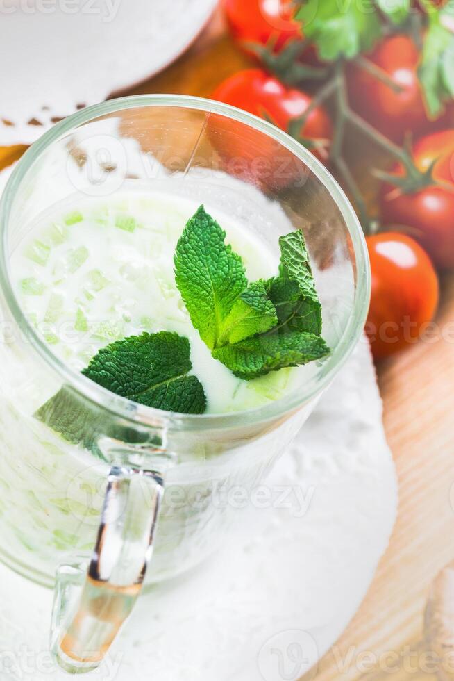 Refreshing mint and yogurt drink served with cherry tomatoes on wooden table photo