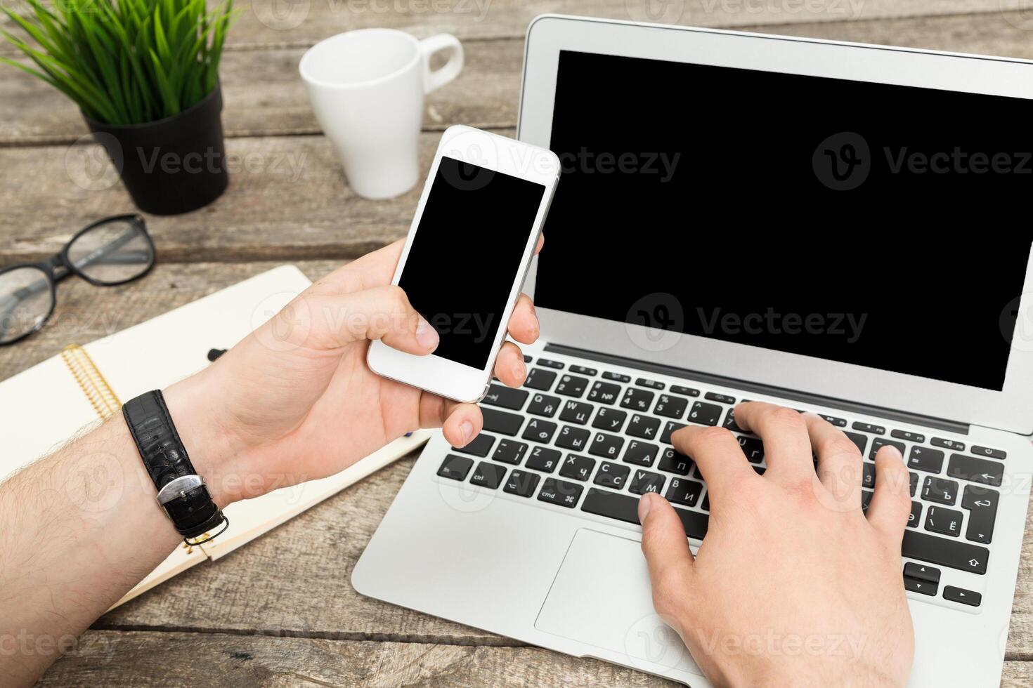 Individual interacting with a laptop and smartphone on a wooden table in a casual workspace setting photo