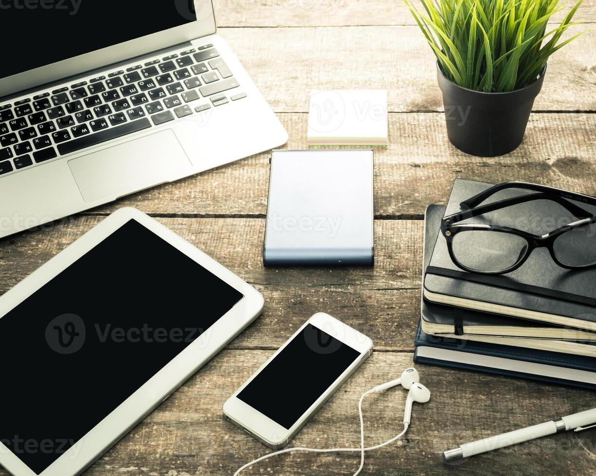 Workspace setup with laptop, smartphone, tablet, and stationary on wooden table in a cozy environment photo