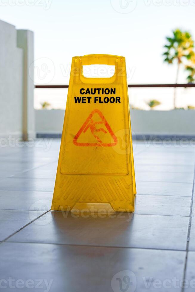 Caution sign indicating wet floor near pool area on a sunny day with palm trees in background photo