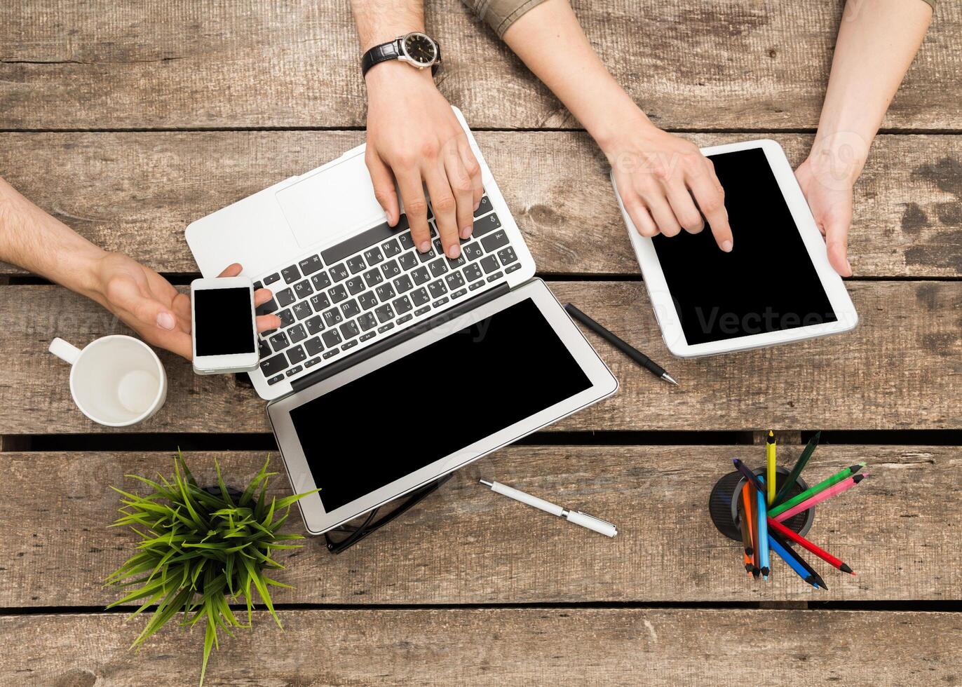 Collaborative workspace featuring multiple devices on a wooden table during a casual meeting photo