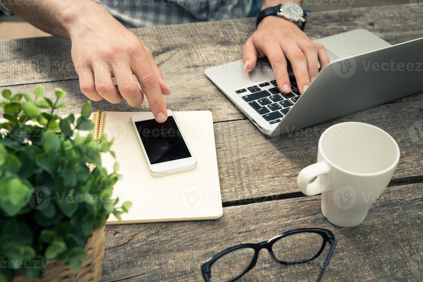 Working on a laptop with smartphone, notebook, and coffee cup on a wooden table in a cozy workspace photo